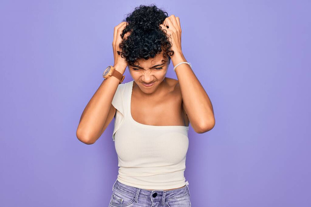 Young beautiful african american afro woman wearing casual t-shirt over purple background suffering from headache desperate and stressed because pain and migraine. Hands on head. - Foto, immagini