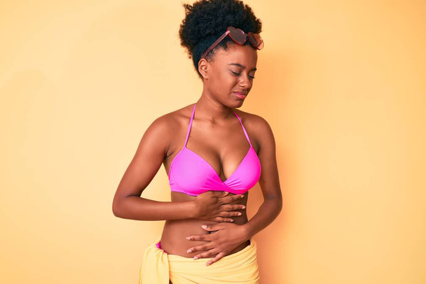 Genç Afro-Amerikalı kadın midesi üstünde bikini giyiyor çünkü hazımsızlık, acı verici bir hastalık kendini iyi hissetmiyor. Ağrı kavramı.  - Fotoğraf, Görsel