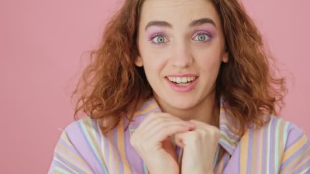 A close-up view of a surprised young woman is looking to the camera isolated over a pink background in studio - Materiał filmowy, wideo