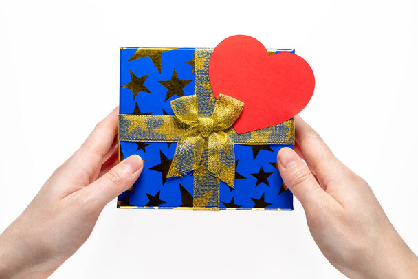 Altın kurdeleli hediye ya da hediye kutusu ve beyaz arka planda kağıt kalp ve kadın eli üst görünümü. - Fotoğraf, Görsel