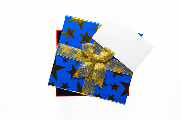 Caja regalo o regalo con cinta dorada y tarjeta de felicitación sobre fondo blanco vista superior
. - Foto, imagen