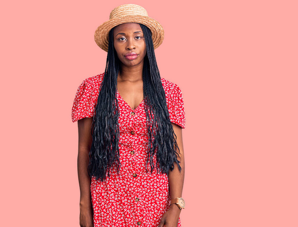 Jeune femme afro-américaine portant un chapeau d'été à l'air endormi et fatigué, épuisé par la fatigue et la gueule de bois, les yeux paresseux le matin.  - Photo, image