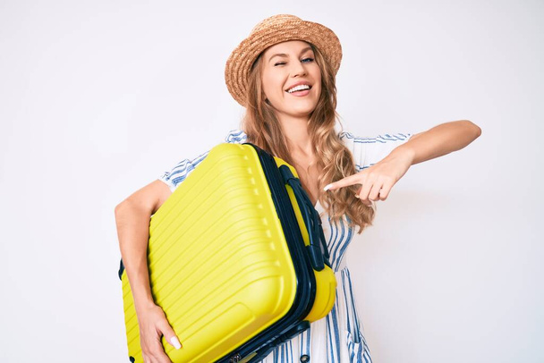 Mulher caucasiana jovem com cabelo loiro usando vestido de verão e segurando saco de cabine piscando olhando para a câmera com expressão sexy, rosto alegre e feliz
.  - Foto, Imagem