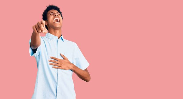 Junger afrikanisch-amerikanischer Mann in lässiger Kleidung lacht dich aus, zeigt mit der Hand über den Körper in die Kamera, schämt sich  - Foto, Bild