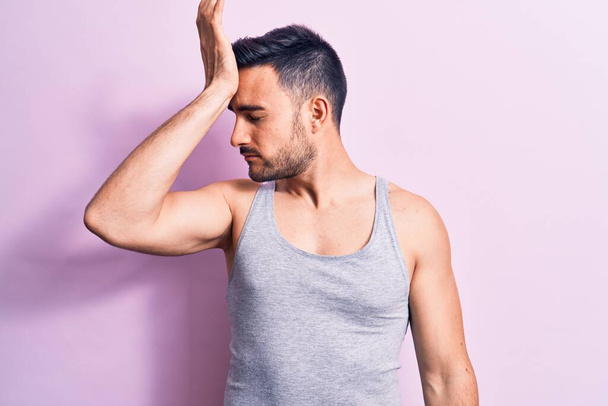 Young handsome man with beard wearing casual sleeveless t-shirt over pink background surprised with hand on head for mistake, remember error. Forgot, bad memory concept. - Фото, зображення