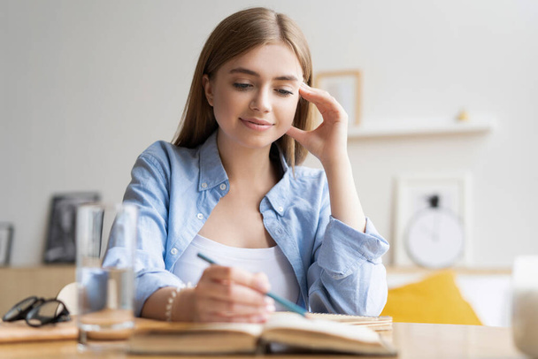 Focused young woman writing letter on table at home office. Concentrated businesswoman making notes in notebook - Foto, Imagem