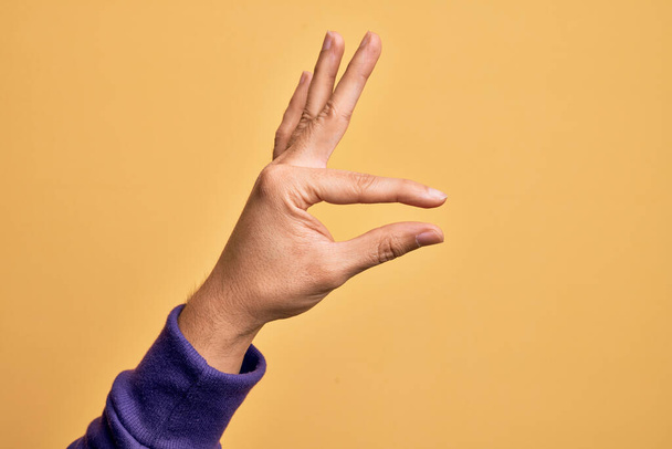 孤立した黄色の背景のピッキングの上に指を示す白人の若者の手と目に見えないものを取ります,空間を示す指でオブジェクトを保持 - 写真・画像
