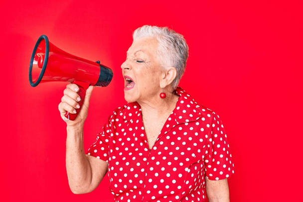 Старша красива жінка з сірим волоссям кричить за допомогою мегафона над ізольованим червоним тлом
 - Фото, зображення