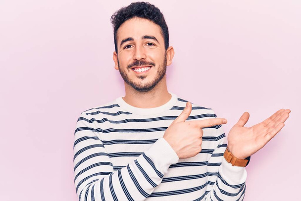 Fiatal spanyol férfi, alkalmi ruhát visel, csodálkozva és mosolyogva a kamerába, miközben bemutatja a kezét és ujjal mutogat.  - Fotó, kép