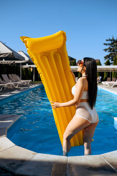 Slanke vrouw met opblaasbare matras aan het zwembad op resort. Mooi meisje ontspannen aan het zwembad in zonnige dag, zomervakantie van aantrekkelijke vrouwelijke persoon - Foto, afbeelding