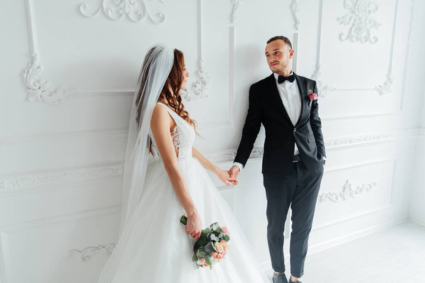 The first meeting of the groom in a black suit and the bride in a white wedding dress with a bouquet in the interior of a photo studio on a white and black background - Фото, зображення