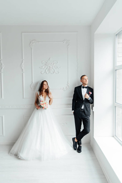 The first meeting of the groom in a black suit and the bride in a white wedding dress with a bouquet in the interior of a photo studio on a white and black background - Photo, Image
