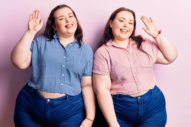 Junge Plus-Size-Zwillinge in lässiger Kleidung verzichten auf ein fröhliches Hallo und lächeln freundliche Willkommensgeste  - Foto, Bild