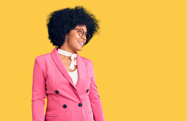 Jeune fille afro-américaine portant des vêtements de travail et des lunettes regardant de côté avec le sourire sur le visage, expression naturelle. riant confiant.  - Photo, image