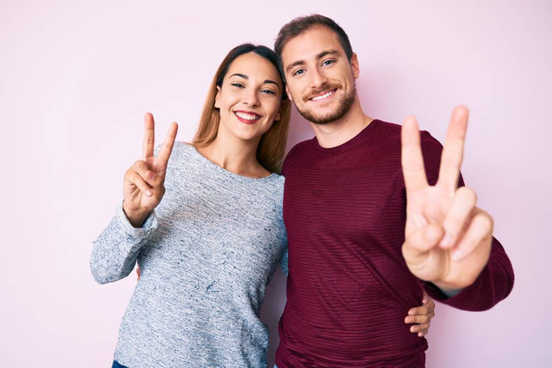 Beautiful couple wearing casual clothes smiling looking to the camera showing fingers doing victory sign. number two.  - Photo, Image