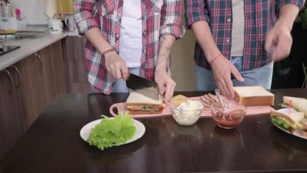 A young couple man and woman make sandwiches in their kitchen. The concept of home-cooked meals on your own. Long-haired fashion guy and girl in the kitchen - Záběry, video