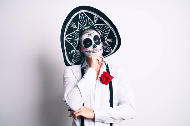 Man wearing day of the dead costume over white serious face thinking about question with hand on chin, thoughtful about confusing idea  - Foto, immagini