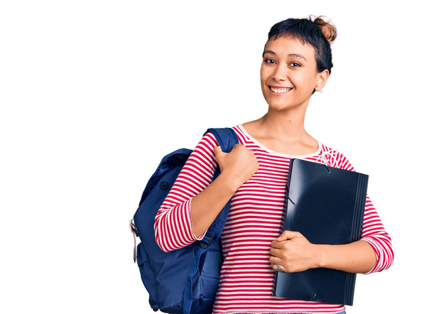 Young woman wearing student backpack holding binder looking positive and happy standing and smiling with a confident smile showing teeth  - Zdjęcie, obraz