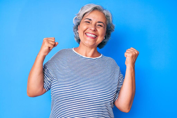 Старшая латиноамериканская седовласая женщина в повседневной одежде очень счастлива и взволнована, делая жест победителя с поднятыми руками, улыбаясь и крича об успехе. празднование концепции.  - Фото, изображение