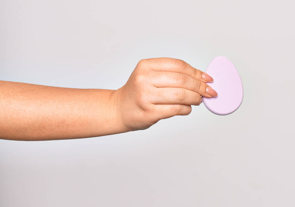 Hand of caucasian young woman holding pink makeup sponge over isolated white background - Fotó, kép