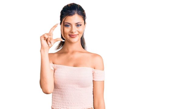 Young beautiful woman wearing casual clothes smiling and confident gesturing with hand doing small size sign with fingers looking and the camera. measure concept.  - Foto, afbeelding