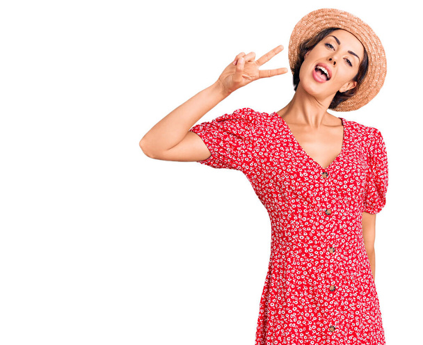 Joven hermosa mujer con sombrero de verano mostrando y señalando hacia arriba con los dedos número dos mientras sonríe confiado y feliz
.  - Foto, Imagen