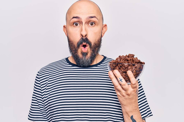 Young handsome man holding chocolate cereals scared and amazed with open mouth for surprise, disbelief face  - Foto, Imagem