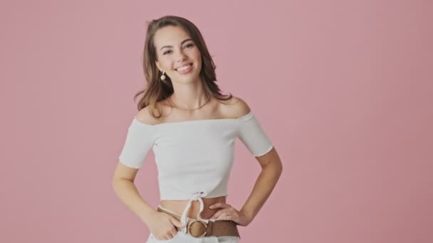 A pretty nice young woman is showing peace gesture with both hands to the camera standing isolated over pink background in studio - Video