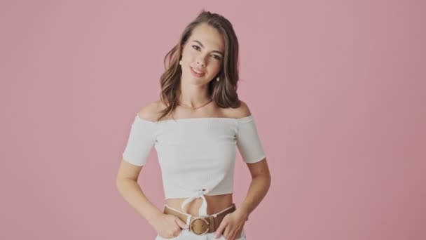 A beautiful young woman is listening to someone and nodding showing thumb up gesture isolated over pink background in studio - Imágenes, Vídeo
