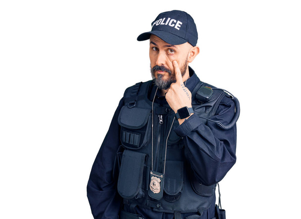 Young handsome man wearing police uniform pointing to the eye watching you gesture, suspicious expression  - Φωτογραφία, εικόνα