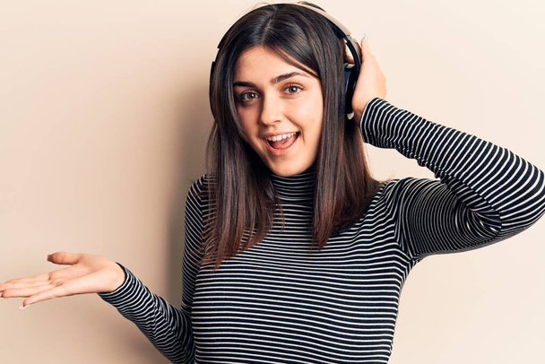 Young beautiful girl listening to music using headphones celebrating achievement with happy smile and winner expression with raised hand  - Photo, Image