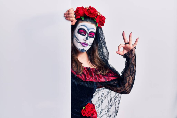 Young woman wearing day of the dead custome holding blank empty banner smiling positive doing ok sign with hand and fingers. successful expression.  - Photo, Image