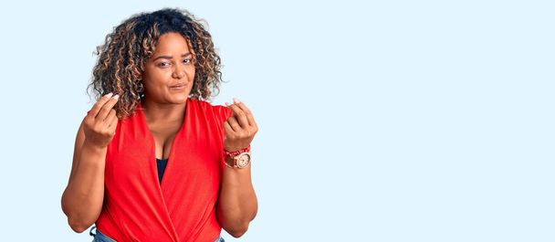 Νεαρή Αφροαμερικάνα συν μέγεθος γυναίκα φορώντας casual στυλ με αμάνικο πουκάμισο κάνει χειρονομία χρήματα με τα χέρια, ζητώντας την πληρωμή του μισθού, εκατομμυριούχος επιχείρηση  - Φωτογραφία, εικόνα