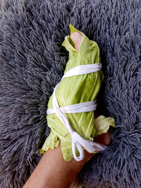 Τυλιγμένα πόδια με λευκά φύλλα λάχανου.Τα φύλλα λάχανου μπορούν να βγάλουν ασθένειες από το σώμα μας. Τυλίγοντας το πόδι σε λάχανο για ανακούφιση του πόνου - Φωτογραφία, εικόνα