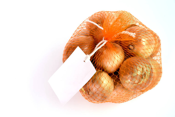 Vista superior de cebollas en bolsa de red con etiqueta blanca colocada sobre fondo aislado
 - Foto, imagen