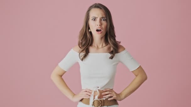 A disappointed young woman is raising her shoulders standing isolated over pink background in studio - Video