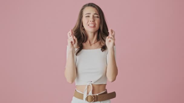 Een mooie jonge vrouw is het maken van een wens tijdens het kruisen van haar vingers staan geïsoleerd over roze achtergrond in studio - Video