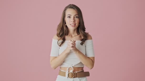 A happy young woman is doing winner gesture and rejoicing standing isolated over pink background in studio - Imágenes, Vídeo