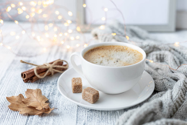 White cup with coffee, knitted scarf and garland on wooden table. Autumn mood. Cozy autumn composition. Hygge concept - Image - Photo, image