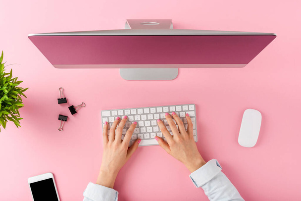 Female hands using modern computer with business accessories on pink background. Office desktop. Top view - Foto, immagini