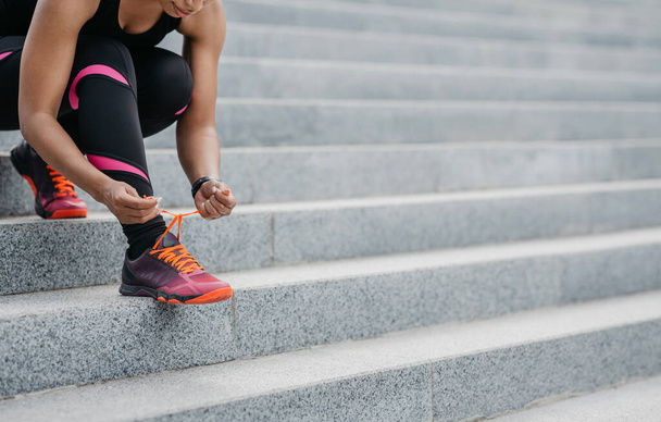 Городская деятельность. Африканская американка в спортивной одежде, завязывающая шнурки на кроссовки для тренировки - Фото, изображение
