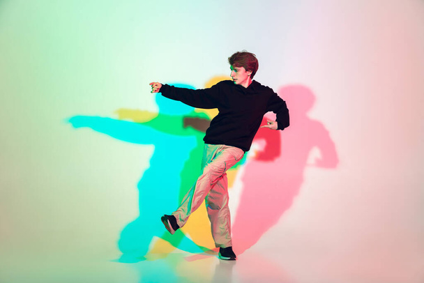Young beautiful man dancing hip-hop, street style isolated on studio background in neon light - Foto, Imagen