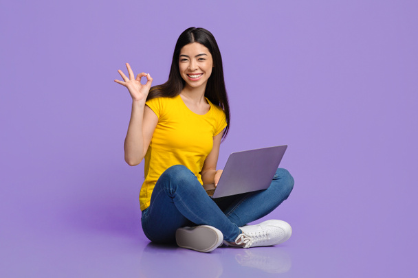 Her şey yolunda, neşeli Asyalı kız dizüstü bilgisayarda oturuyor ve iyi işareti gösteriyor. - Fotoğraf, Görsel