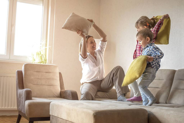A caucasian woman playing with pillows with her 4-year-old son and 6-year-old daughter on the couch in their home - Photo, Image