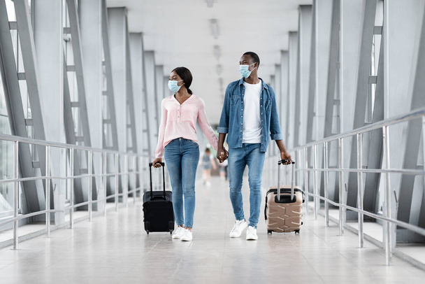 Reprise du vol. Couple noir portant des masques protecteurs marchant avec des valises à l'aéroport - Photo, image