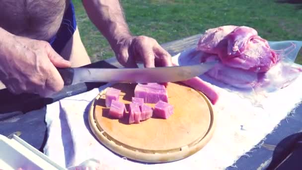 Мужик режет свинину для гуляша. Кубики и нарезанные куски свинины на деревянной доске. Хорошее свежее мясо - Кадры, видео