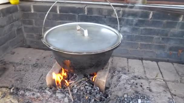 Nagyapa száraz nyírfát tesz egy üst alá alumínium fedéllel. Kerti főzés fehér tégla tűzhely. - Felvétel, videó