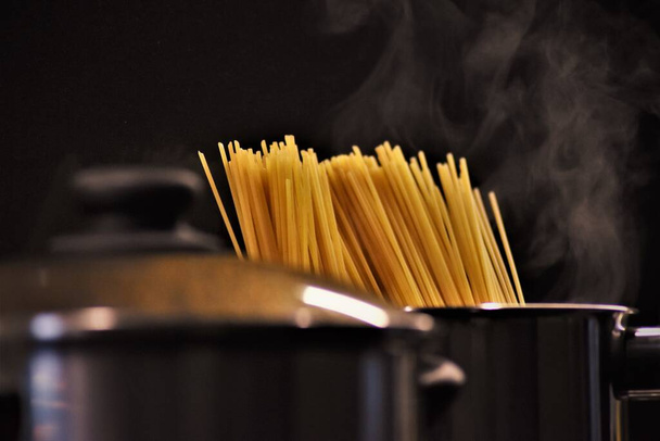 A closeup of uncooked pasta in a pot with boiling water under the lights - Фото, зображення