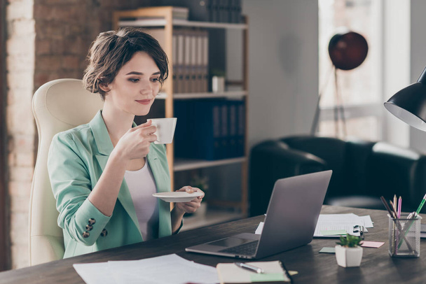 Profile photo of attractive business lady look notebook table watch webinar hold hot fresh coffee cup mug good mood distance home remote work sit chair modern interior office indoors - Photo, Image