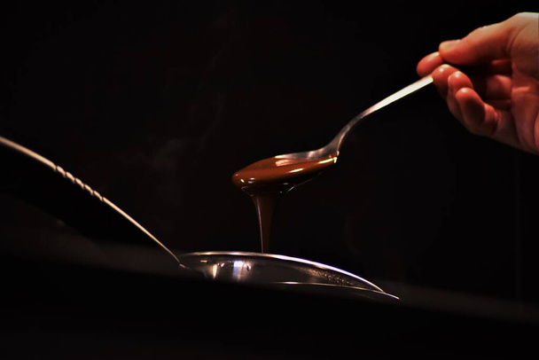 A closeup of a person picking hot melted chocolate with a spoon on a dark background - Foto, Bild